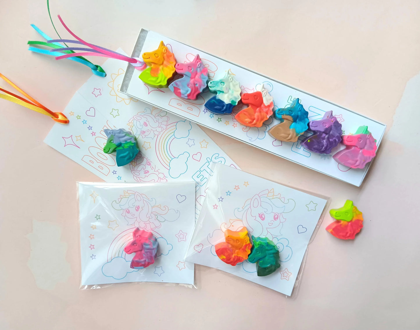 Multicolored unicorn-shaped crayons, each with unique color swirls, packaged in a gift-ready box or small favor bags with a coloring card or bookmark. Perfect for party favors or creative play. Available exclusively at rainbowsanddreamsshop.com.