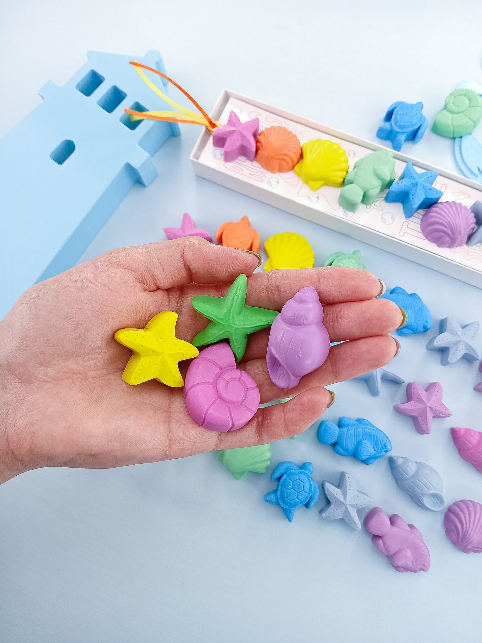 Hand holding colorful sea creature crayons in pastel rainbow hues, non-toxic handmade USA gift for children.